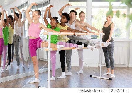 Teenage girl doing leg stretching exercise holding by ballet barre during dance courses 129857351