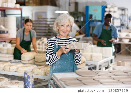Portrait of craftswoman in a production workshop among ceramic cups and plates 129857359