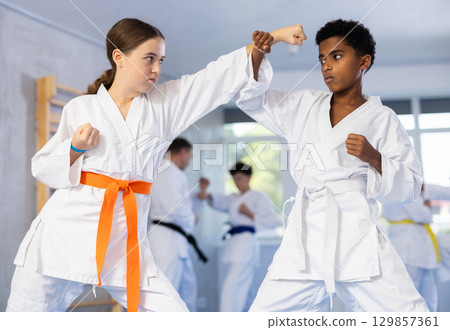 Teen girl karateka honing punches in kumite with african boy 129857361