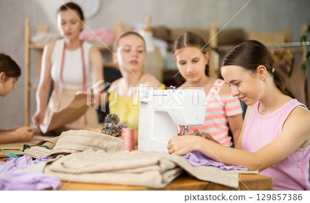 Girl child watches female classmates sew and creating clothes 129857386