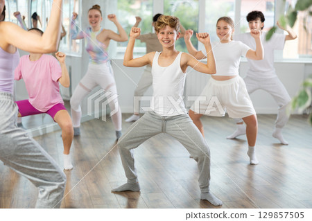 Male boy student repeats movements of unrecognizable teacher during group modern dance class. 129857505