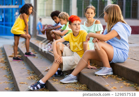 Positive tweenagers friendly blabbing while sitting on steps outdoors Positive tweenagers friendly blabbing while sitting on steps outdoors 129857518