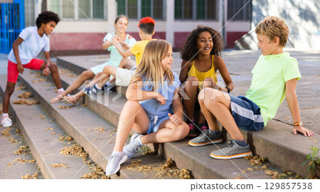 Group of boys and girls sitting on stairs outdoors and chatting 129857538
