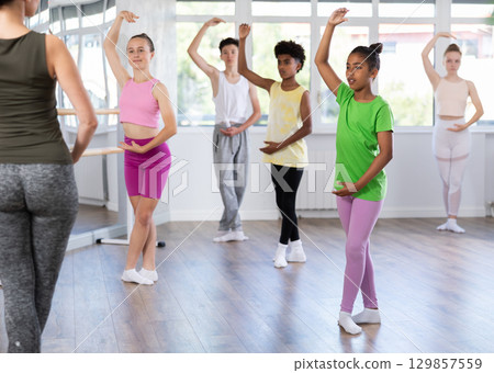 Thin teenage girl practicing fifth position of ballet standing in row with others 129857559