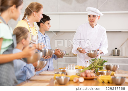 Cooking class, culinary, food and people concept - happy group of children and male chef cook cooking in modern kitchen 129857566
