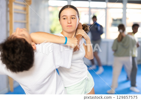 Tween girl practicing hand blocking with elbow strike to chin during training sparring with boy Tween girl practicing hand blocking with elbow strike to chin during training sparring with boy 129857575