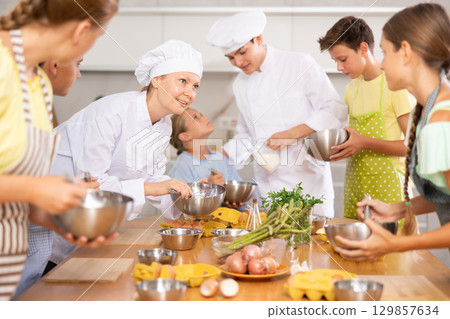 During cooking lesson, female cook tells children about culinary rules, guy assistant helps child 129857634