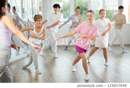 Female girl student repeats movements of unrecognizable teacher during group modern dance class. Female girl student repeats movements of unrecognizable teacher during group modern dance class. 129857646