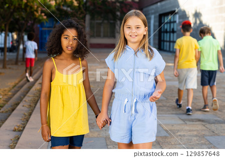 Positive girls walking together through alley during summer day 129857648