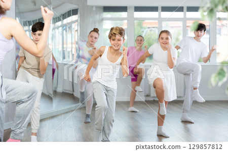 Male boy student repeats movements of unrecognizable teacher during group modern dance class. Male boy student repeats movements of unrecognizable teacher during group modern dance class. 129857812