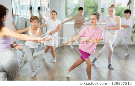 Young girls and boys repeat the movements of dance teacher, training in spacious studio Young girls and boys repeat the movements of dance teacher, training in spacious studio 129857813