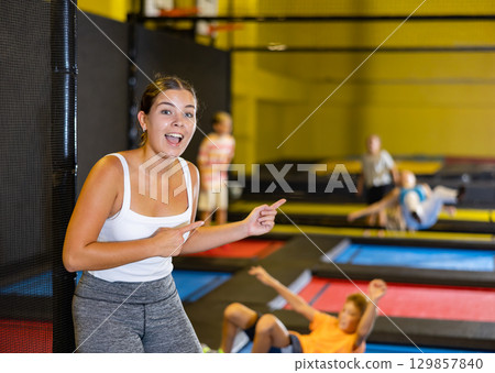 Happy young European female in white top and gray leggings posing on trampolines during active weekend free time in entertainment center 129857840