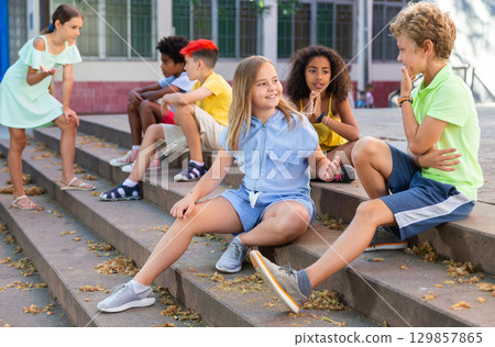 Positive tweenagers friendly blabbing while sitting on steps outdoors Positive tweenagers friendly blabbing while sitting on steps outdoors 129857865