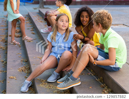 Children talking together while sitting on stairs outdoors 129857882