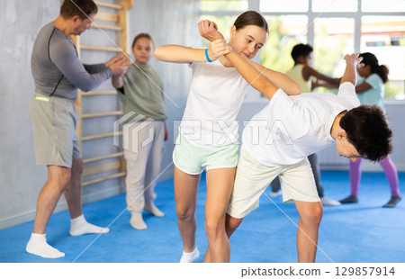 Tween girl practicing painful armlock in training bout with boy during self defence course 129857914