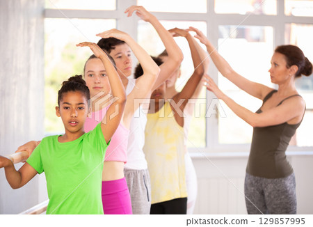 Black teen girl mastering third position at barre in ballet studio Black teen girl mastering third position at barre in ballet studio 129857995