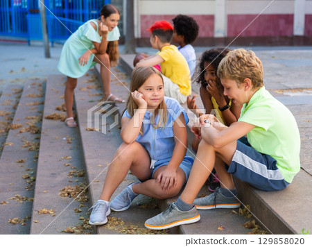 Happy tweenagers friends sitting on steps outdoors and chatting Happy tweenagers friends sitting on steps outdoors and chatting 129858020