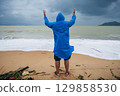 back of male tourist in a raincoat on dirty beach by the sea after a storm in cloudy weather. Concept of the rainy and monsoon season 129858530