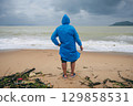 back of man tourist in a raincoat on a dirty beach by the sea after a storm in cloudy weather. The concept of the rainy and monsoon season 129858531