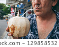 elderly male tourist drinks a drinking coconut through a straw on vacation on treet 129858532