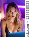 Beautiful sexy young female webcam model in lingerie chats and sexting online on laptop on bed in bedroom 129858535