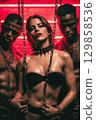 Sexy mistress woman with two submissive men in chains. BDSM sex with submission and domination 129858536