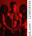 dominant sexual man with two submissions women bound by chains. The concept of BDSM sex with domination and submission 129858544