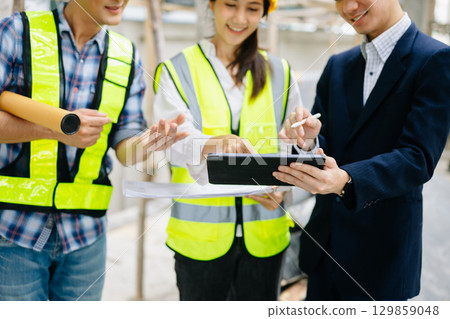 Contractor and architect looking at plan, tablet, laptop and talking about working on big project. Contractor and architect looking at plan, tablet, laptop and talking about working on big project. 129859048