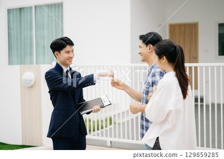 Asian man Real estate broker agent showing a house detail in her file to the young Asian couple lover looking and interest to buy it. Asian man Real estate broker agent showing a house detail in her file to the young Asian couple lover looking and interest to buy it. 129859285