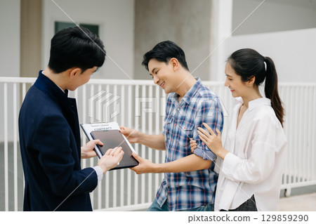 Asian man Real estate broker agent showing a house detail in her file to the young Asian couple lover looking and interest to buy it. Asian man Real estate broker agent showing a house detail in her file to the young Asian couple lover looking and interest to buy it. 129859290
