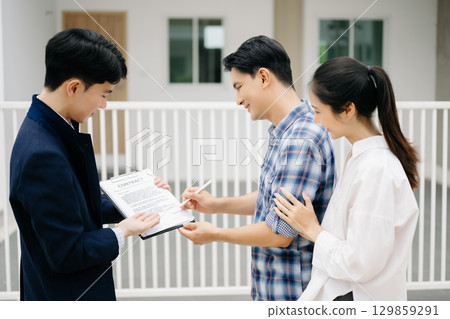 Asian man Real estate broker agent showing a house detail in her file to the young Asian couple lover looking and interest to buy it. Asian man Real estate broker agent showing a house detail in her file to the young Asian couple lover looking and interest to buy it. 129859291