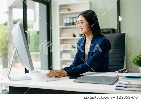 Asian woman sitting at a desk using a laptop computer Navigating Finance and Marketing 129859476