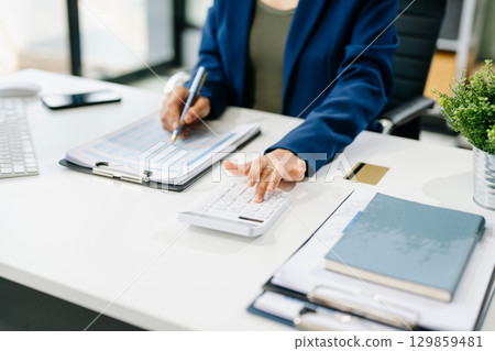 Women counting coins on calculator taking from the piggy bank. hand holding pen working on calculator Women counting coins on calculator taking from the piggy bank. hand holding pen working on calculator 129859481