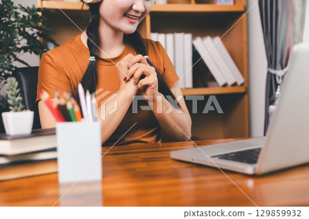 Asian girl doing homework and studying at home. woman using laptop at desk write notes watching webinar, study online, look at learn web class or having virtual call meeting remote working from home. Asian girl doing homework and studying at home. woman using laptop at desk write notes watching webinar, study online, look at learn web class or having virtual call meeting remote working from home. 129859932