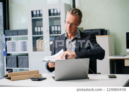 Professional businessman working at office with laptop, tablet, and notes. Perfect for business, finance, accounting Professional businessman working at office with laptop, tablet, and notes. Perfect for business, finance, accounting 129860438