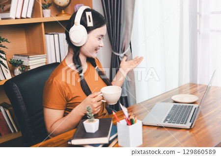 Asian girl doing homework and studying at home. woman using laptop at desk write notes watching webinar, study online, look at learn web class or having virtual call meeting remote working from home. 129860589