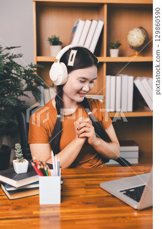Asian girl doing homework and studying at home. woman using laptop at desk write notes watching webinar, study online, look at learn web class or having virtual call meeting remote working from home. Asian girl doing homework and studying at home. woman using laptop at desk write notes watching webinar, study online, look at learn web class or having virtual call meeting remote working from home. 129860590