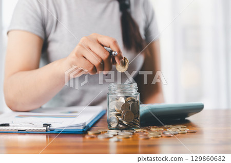 Businesswoman saving money with piggy bank and coins on desk, financial planning and investment concept. Young Asian woman making stack of coin. invest save finance concept, saving money, investment 129860682