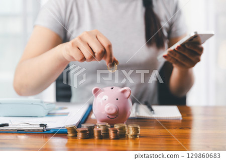 Businesswoman saving money with piggy bank and coins on desk, financial planning and investment concept. Young Asian woman making stack of coin. invest save finance concept, saving money, investment 129860683
