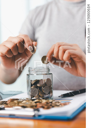 Businesswoman saving money with piggy bank and coins on desk, financial planning and investment concept. Young Asian woman making stack of coin. invest save finance concept, saving money, investment 129860684
