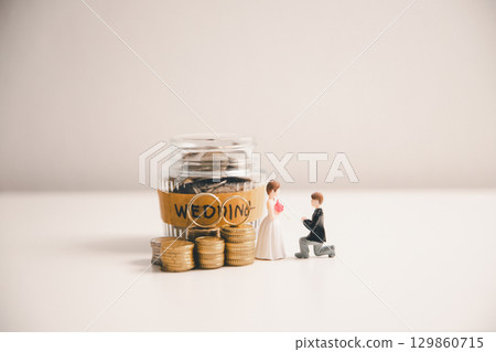 Save money for wedding and planning wedding concept. Sustainable financial goal for family life or married life. Miniature wedding on rows of rising coins, depicts savings or growth for new family. 129860715