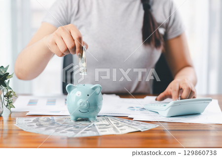Businesswoman saving money with piggy bank and coins on desk, financial planning and investment concept. Young Asian woman making stack of coin. invest save finance concept, saving money, investment 129860738