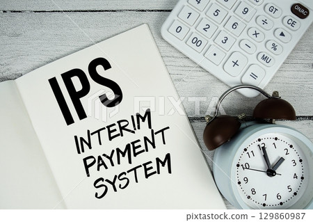 IPS Interim Payment System text on paper notebook page with alarm clock and calculator on wooden background 129860987