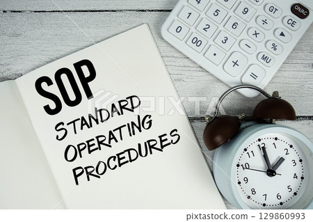 SOP Standard Operating Procedures text on paper notebook page with alarm clock and calculator on wooden background 129860993