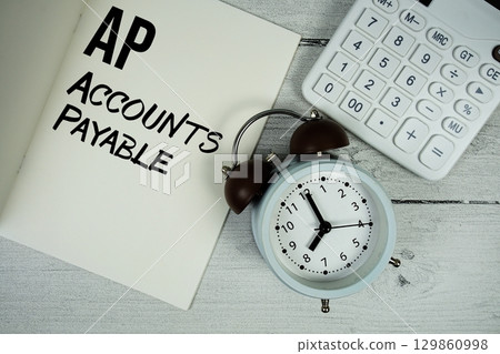 AP Advance Payment text on paper notebook page with alarm clock and calculator on wooden background 129860998