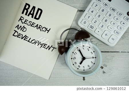 Research and Development text on paper notebook page with alarm clock and calculator on wooden background 129861012