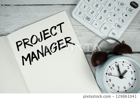 PROJECT MANAGER text on paper notebook page with alarm clock and calculator on wooden background PROJECT MANAGER text on paper notebook page with alarm clock and calculator on wooden background 129861041