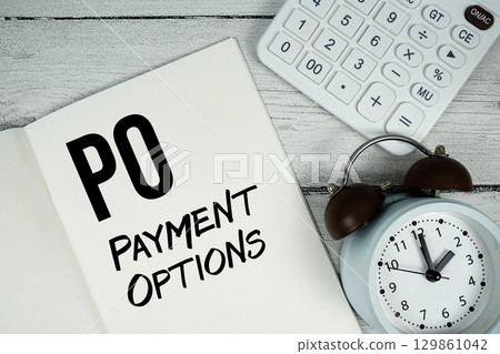 PO Payment Options text on paper notebook page with alarm clock and calculator on wooden background 129861042