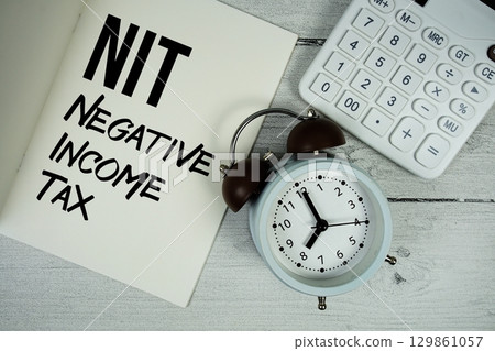 NIT Negative Income Tax text on paper notebook page with alarm clock and calculator on wooden background 129861057