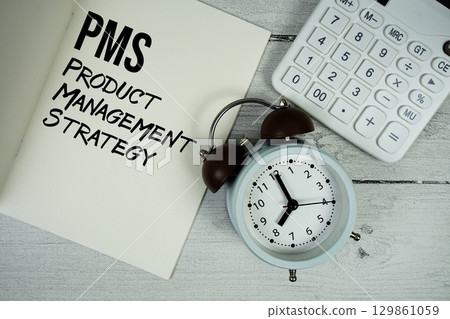 PMS Product Management Strategy text on paper notebook page with alarm clock and calculator on wooden background 129861059